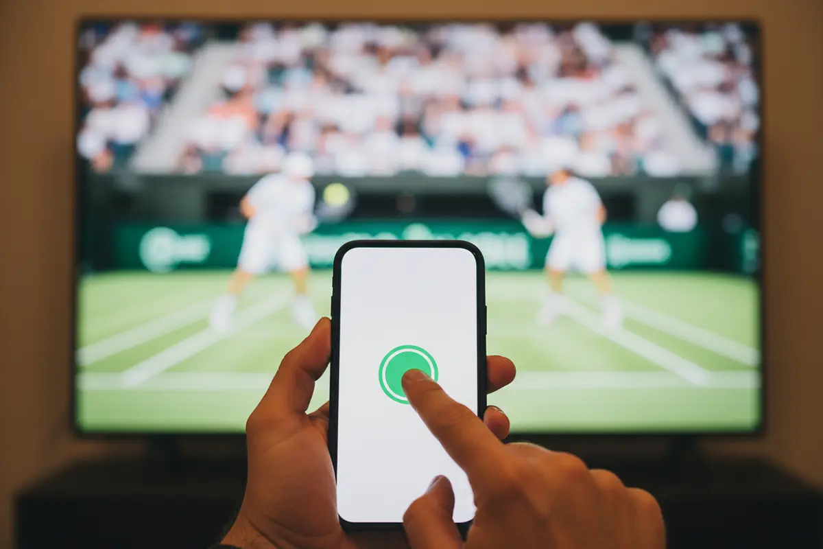 Mano pulsando un botón en la pantalla de un móvil durante un partido de tenis
