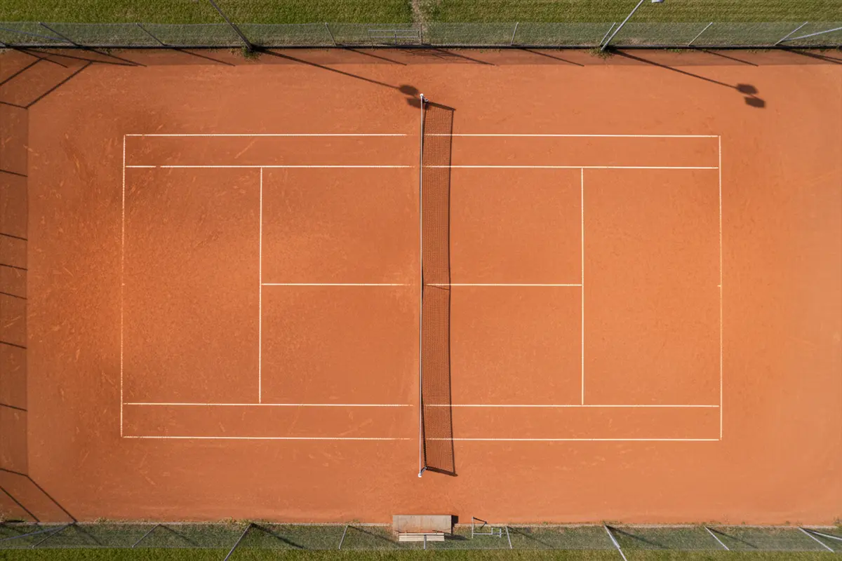 Vista cenital de una pista de tenis de tierra batida con líneas marcadas
